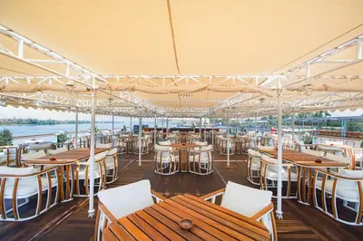 a restaurant with wooden tables and white chairs at Sonesta St George Nile Cruise - Luxor to Aswan 4 Nights from Monday to Friday in Luxor