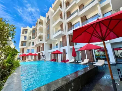 a swimming pool in front of a building with red umbrellas at 2 Bed Resort Apt-Sleeps 4-Balcony-Hotel Services in Hurghada