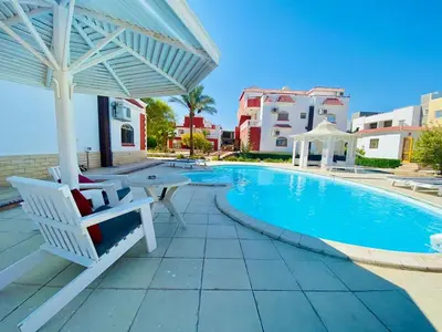 a swimming pool with a white umbrella and a table and chairs at Moubark 6 Directly to the swimming pool in Hurghada