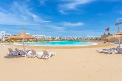 a group of chairs and umbrellas on a beach at New! Lovely 1BR in Swan Lake, Gouna. Azure Lagoon in Hurghada