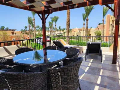 a patio with a table and chairs and palm trees at Chalet Stella Makadi Beach 5* in Hurghada