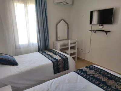 a bedroom with two beds and a mirror and a tv at Chalet Stella Makadi Beach 5* in Hurghada