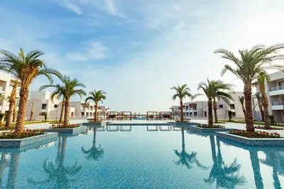 a swimming pool with palm trees and buildings at JAZ Elite Amara in Marsa Alam City
