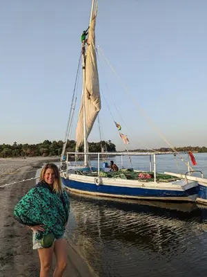 a woman standing next to a boat in the water at Felucca sailing overnight experience with imaginative felucca aswan in Aswan