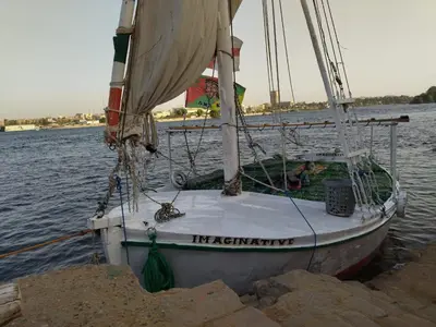 a sail boat docked on the shore of the water at Felucca sailing overnight experience with imaginative felucca aswan in Aswan
