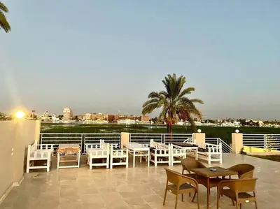 a patio with white chairs and tables and a view at Royal Nile Villa - Luxury Nile View Apartment 1 in Luxor