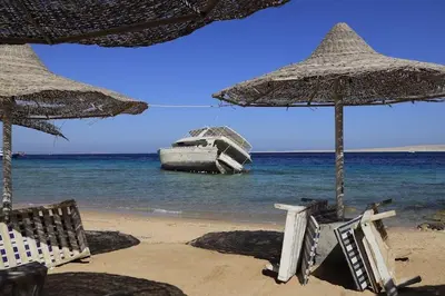 a boat in the ocean with chairs and umbrellas on a beach at Charming Marina Crib Pool Beach Gym Spa in Hurghada