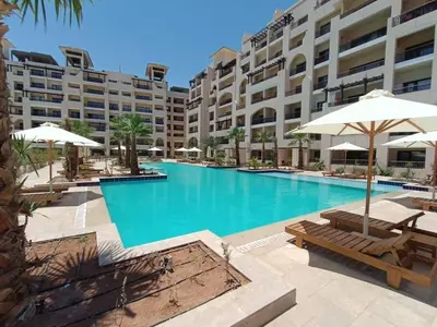 a large swimming pool with benches and umbrellas in front of a building at 3316- Awesome Garden view studio in Al Dau Heights in Hurghada
