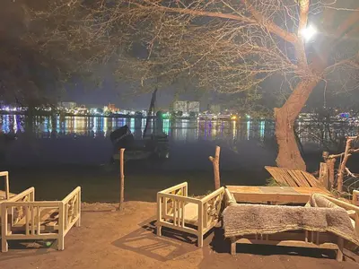 a table and chairs next to a lake at night at Salatoos Mango Garden and Guesthouse in Aswan