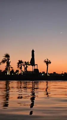 a statue in front of a sunset with palm trees at El Gouna Mangroovy Residence Sea View - kitesurfing in Hurghada