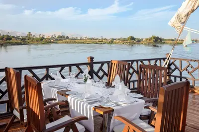 a table set up on a deck with a view of a river at Farouz El Nil I Nile Cruise - Every Monday from Luxor for 07 & 05 Nights in Ţawd