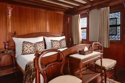 a bedroom with a bed and a table and a chair at JAZ Farouz El Nil III Nile Cruise - Every Saturday from Luxor for 07 & 05 Nights in Luxor