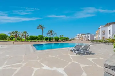 a swimming pool with two chairs and a building at Cozy 2BR in Cyan, El Gouna Swiming Pool Access in Hurghada