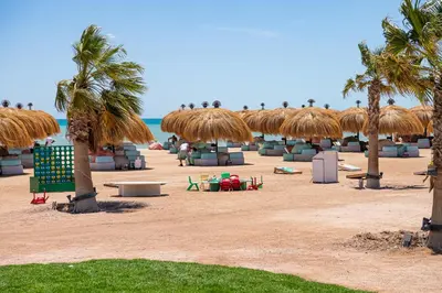 a sandy beach with palm trees and straw umbrellas at Modern apartment with large pool & beach access in Hurghada