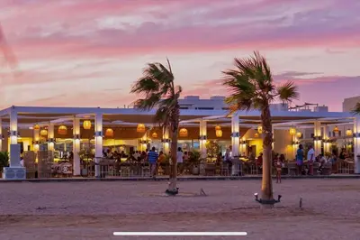 a restaurant on the beach with palm trees in front at Modern apartment with great Pool & Beach access in Hurghada