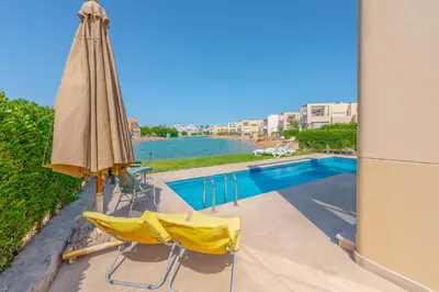 a patio umbrella and chairs next to a swimming pool at Elegant 4BR in Tawila, Gouna. Private Pool, Lagoon in Hurghada