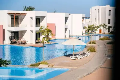a swimming pool with chairs and an umbrella and some buildings at Makadi Heights Elite Worldwide Residences - Hurghada, Egypt in Hurghada