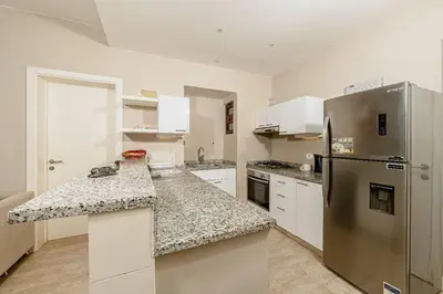 a kitchen with white cabinets and a stainless steel refrigerator at Sabina Lagoon view 2BR Apartment in Hurghada