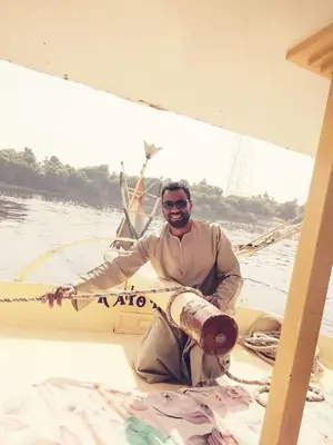 a man sitting on a boat in the water at Aswan Felucca sailing boat and Hotel in Aswan