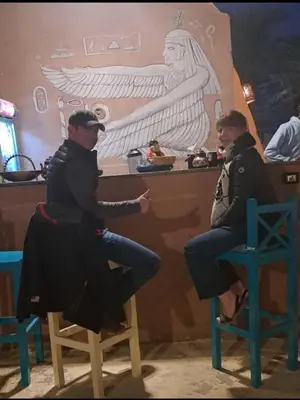 two men sitting in chairs in front of a bar at Miskaa Nubian House in Naj‘ Tinjār