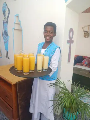 a man holding a tray of orange juice at Miskaa Nubian House in Naj‘ Tinjār