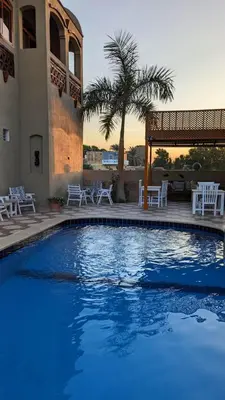 a swimming pool with white chairs and a building at Yasmine Guest House in Luxor