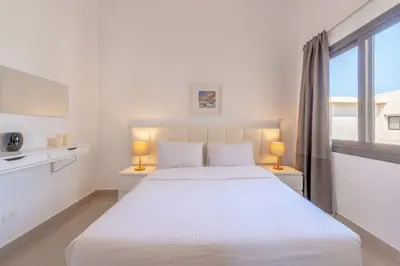 a white bedroom with a large bed and a window at Gcribs apartment pool view in El Gouna