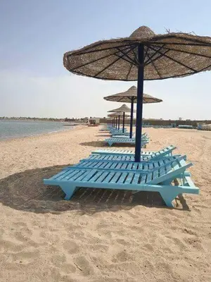 a row of blue lounge chairs under an umbrella on the beach at Harmony Sunny Chalet With Wi-Fi in Hurghada