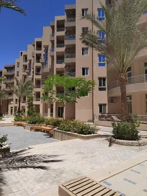 a large apartment building with palm trees and benches at Velký apartmán Princess Resort Hurghada in Hurghada