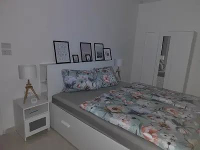 a white bedroom with a bed and a night stand at Velký apartmán Princess Resort Hurghada in Hurghada