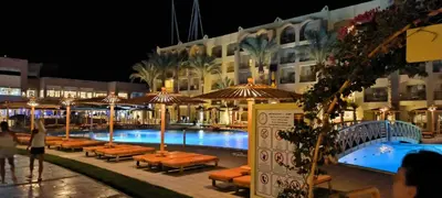 a swimming pool with tables and umbrellas next to a building at Go Egypt Apartments Inside Karma Beach Resort North Al Ahiaa , Hurghada in Hurghada