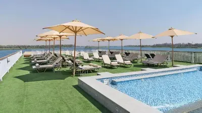 a pool with chairs and umbrellas next to the water at book Now Nile Cruise From Aswaon every Friday & Monday & wednesday in Aswan