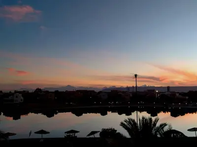 a sunset over a body of water with umbrellas at Soulful 1BR in Italian Compound / Nubia, El Gouna in Hurghada