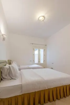 a white bedroom with a large bed with two lights at Abutig Marina flat ground floor in Hurghada