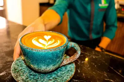 a person holding a blue cup of coffee on a table at Studio Sleeps 2 with Balcony Pool & Parking in Hurghada