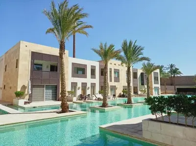 a swimming pool with palm trees in front of a building at one bedroom scarab club el gouna in Hurghada