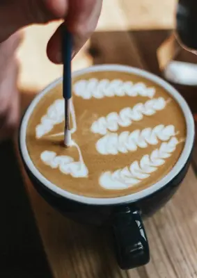 a person sprinkling whipped cream on a cup of coffee at جوليانا بيتش ريزورت in Hurghada
