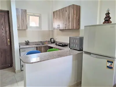 a kitchen with a white refrigerator and wooden cabinets at 2 bedrooms cozy flat at makadi heights in Hurghada