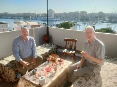 two men sitting on a balcony with a table with food at Ezzo Nubian guest house in Aswan