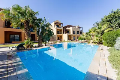 a large blue swimming pool with palm trees and a building at Wonderful apartment with prime location & pool in Hurghada
