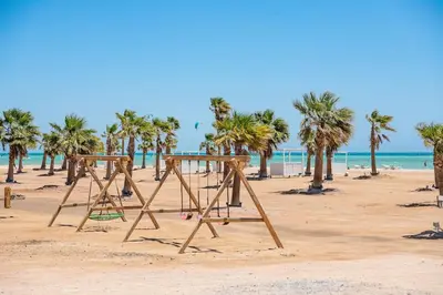 a swing set on a beach with palm trees at Cozy 1 Bedroom Ground Floor Apartment with Pool in Hurghada