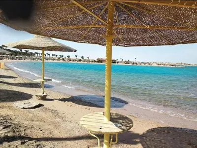 two straw umbrellas and a chair on a beach at 2 bedroom modern flat at Makadi heights in Hurghada