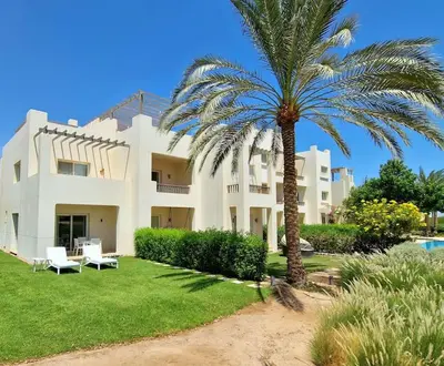 a large white building with a palm tree in front of it at Cheerful space with a huge garden and pool in Hurghada