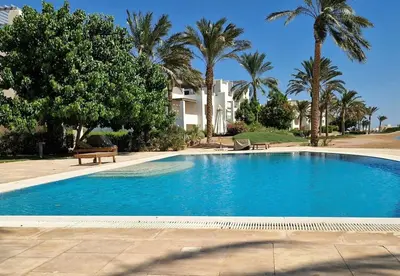 a large blue swimming pool with palm trees and a building at Cheerful space with a huge garden and pool in Hurghada