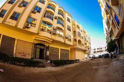 a large yellow building on a dirt road next to a street at Inter Prime apartment 2 in Hurghada