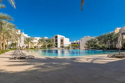 a swimming pool with chairs and palm trees and buildings at Cozy 1BR Apartment in Mangroovy with pool in Hurghada