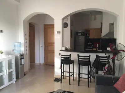 a living room with a kitchen and a bar with stools at Modernes Apartment in El Gouna - South Marina in El Gouna