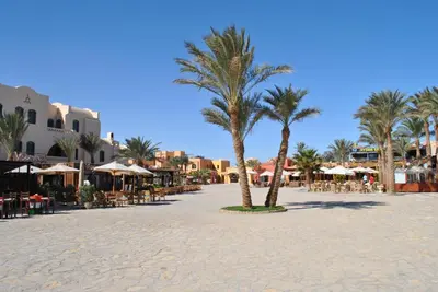 a beach with palm trees and tables and umbrellas at Modernes Apartment in El Gouna - South Marina in El Gouna