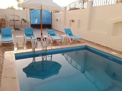a swimming pool with chairs and an umbrella at Nille and Garden View Apartment in Jazīrat al ‘Awwāmīyah