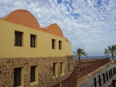 a building on the beach with palm trees in the background at Rohanou Beach Resort in Quseir